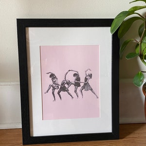 May include: A framed black and white illustration of five people dancing in a line. The people are wearing short skirts and are posed in a dynamic, energetic way. The background is a light pink color.