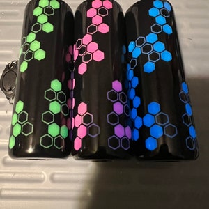 Puede incluir: Tres vasos negros con un patr&oacute;n geom&eacute;trico de panal. Los vasos est&aacute;n decorados con acentos verdes, rosas y azules.