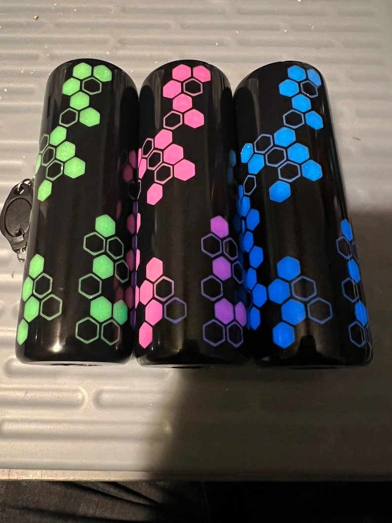 Puede incluir: Tres vasos negros con un patr&oacute;n geom&eacute;trico de panal. Los vasos est&aacute;n decorados con acentos verdes, rosas y azules.