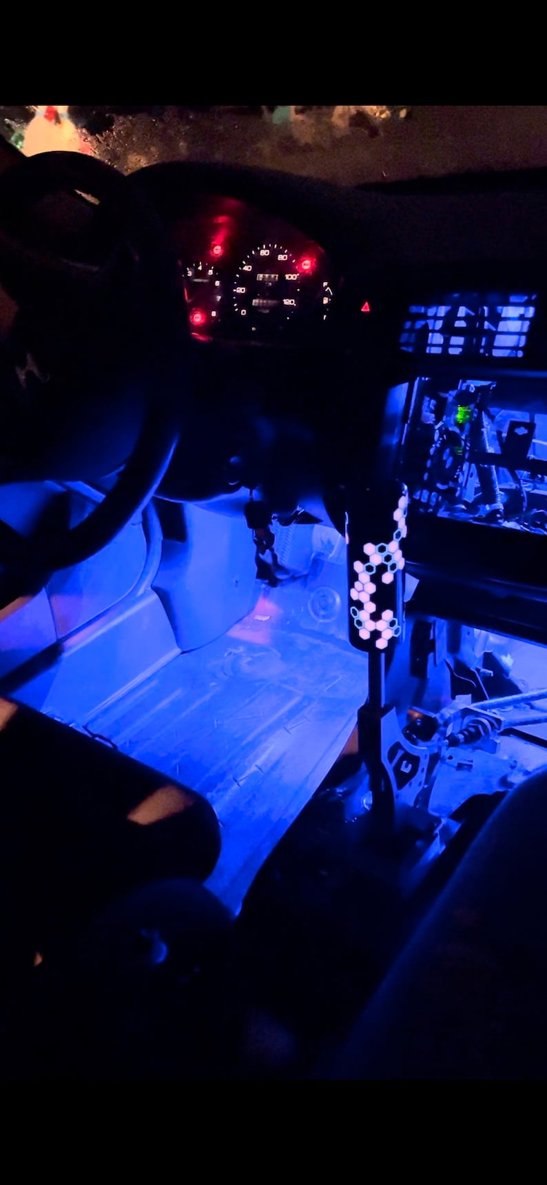 Puede incluir: El interior de un coche con luces LED azules que iluminan el suelo y el salpicadero. El salpicadero tiene un veloc&iacute;metro y otros indicadores. Se ve una palanca de cambios con un patr&oacute;n hexagonal.