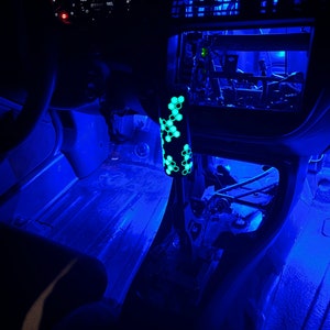 Puede incluir: El interior de un coche con luces LED azules que iluminan el suelo y el salpicadero. Se puede ver una palanca de cambios verde y negra con un patr&oacute;n de panal.