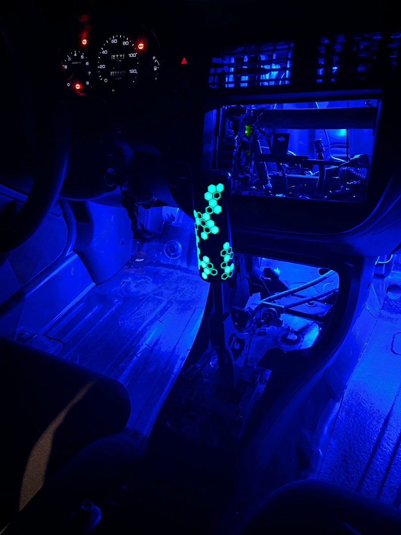Puede incluir: El interior de un coche con luces LED azules que iluminan el suelo y el salpicadero. Se puede ver una palanca de cambios verde y negra con un patr&oacute;n de panal.