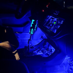 Puede incluir: El interior de un coche con luces LED azules que iluminan el salpicadero, la consola central y el suelo. Se ve una palanca de cambios negra con un patr&oacute;n de panal.