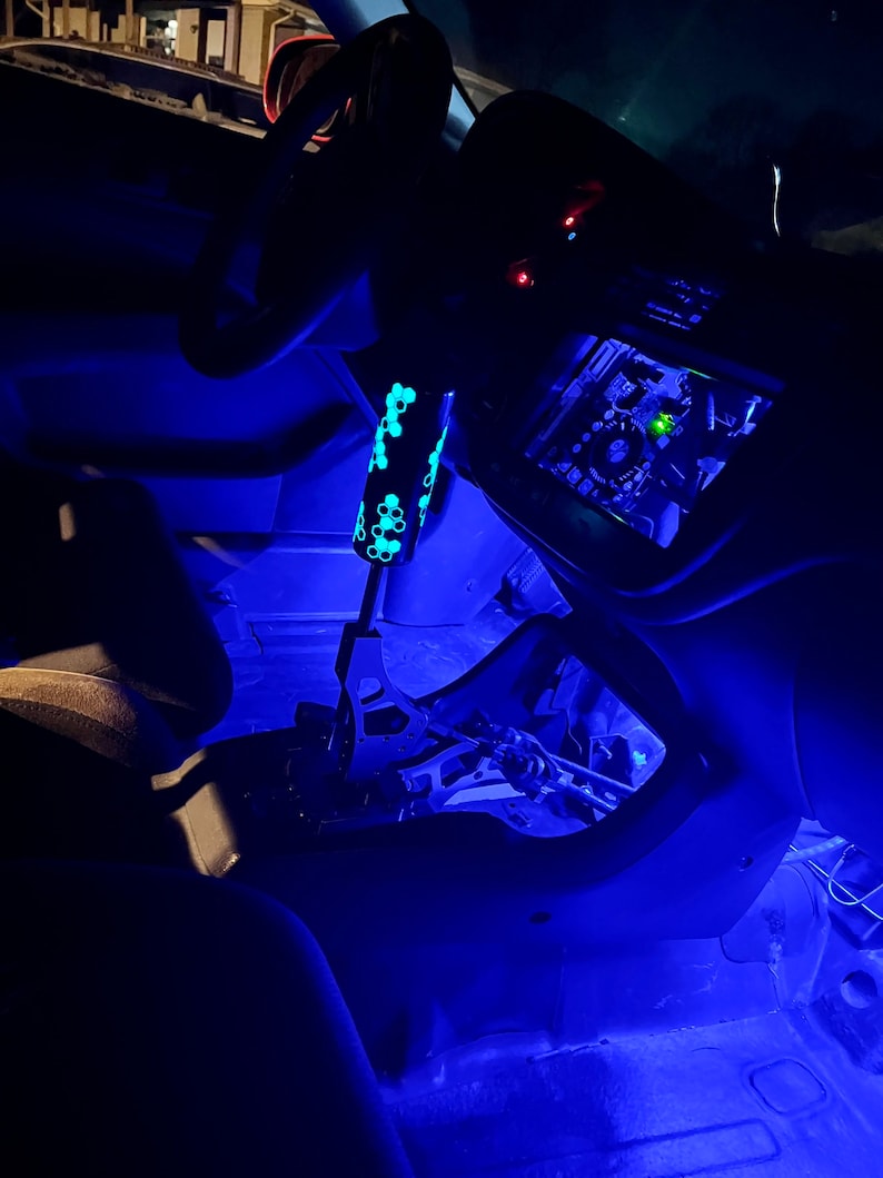 Puede incluir: El interior de un coche con luces LED azules que iluminan el salpicadero, la consola central y el suelo. Se ve una palanca de cambios negra con un patr&oacute;n de panal.