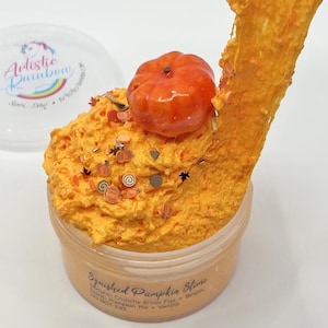 Op de afbeelding: Een oranje slijm in een doorzichtige plastic container, bekroond met een kleine oranje pompoen en decoratieve sprinkles. De container heeft de tekst "Squished Pumpkin Slime" en "DO NOT EAT".