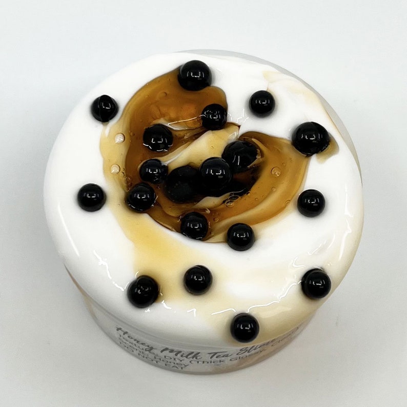May include: A close-up of a white jar with a brown swirl and black boba pearls. The jar is labeled "Honey Milk Tea Slime" with the text "Handmade DIY (Thick Glossy No Heat".