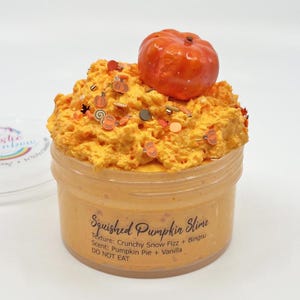 Op de afbeelding: Een pot oranje "Squished Pumpkin Slime" met een pompoendecoratie. De slijm is getextureerd met sprinkles. Het etiket luidt "Texture: Crunchy Snow Fizz + Bingsu, Scent: Pumpkin Pie + Vanilla, DO NOT EAT."