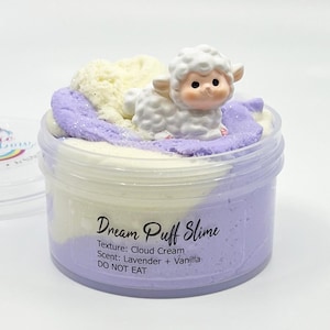 May include: A clear plastic container of Dream Puff Slime. The slime is a mix of lavender, white, and cream colors, topped with a small white lamb figurine. The text on the container reads "Dream Puff Slime", "Texture: Cloud Cream", "Scent: Lavender + Vanilla", and "DO NOT EAT".