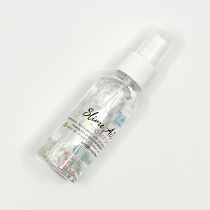 May include: A clear plastic bottle with a white spray nozzle. The bottle is labeled "Slime Art" and has the text "DO NOT DRINK" on it. The bottle contains a clear liquid with colorful glitter and other embellishments.