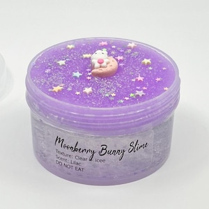 May include: A clear slime in a plastic container with a purple lid. The lid is decorated with glitter, star-shaped sprinkles, and a bunny on a crescent moon. The text "Moonberry Bunny Slime" is printed on the container.