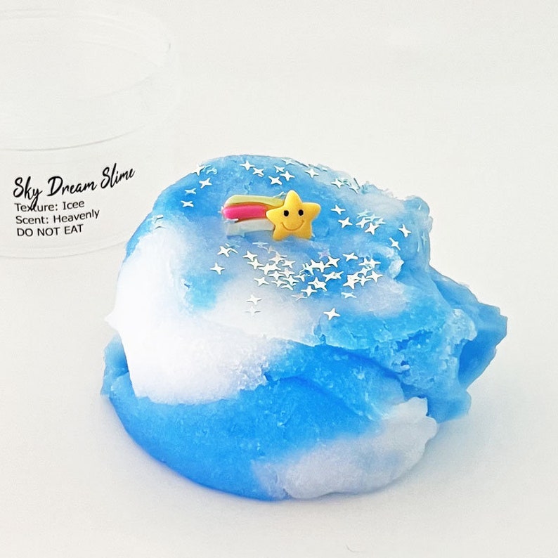 Op de afbeelding: Blauwe en witte slijm met een gele ster en een regenboog erop. De slijm is gelabeld "Sky Dream Slime" met de tekst "Texture: Icee Scent: Heavenly DO NOT EAT".