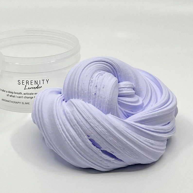 May include: A lavender-coloured slime in a clear container. The slime is soft and fluffy, and it has a calming scent. The container has a label that says "Serenity Lavender" and "Aromatherapy Slime".