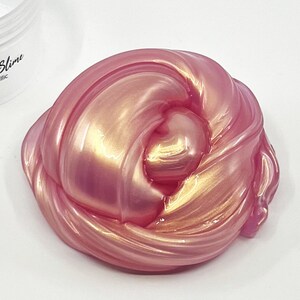 Peut inclure: Gros plan sur une slime rose et or avec une finition chatoyante. La slime est douce et gluante, et elle a l'air amusante &agrave; manipuler.