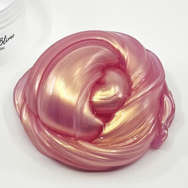 Peut inclure: Gros plan sur une slime rose et or avec une finition chatoyante. La slime est douce et gluante, et elle a l'air amusante &agrave; manipuler.