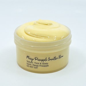 May include: A yellow mango pineapple smoothie slime in a clear plastic container with a black label that reads "Mango Pineapple Smoothie Slime", "Texture: Thick & Glossy", "Scent: Mango Pineapple", and "DO NOT EAT".
