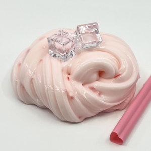 May include: Pink slime with red flecks, topped with two clear plastic ice cubes. A pink heart-shaped straw is in the background.