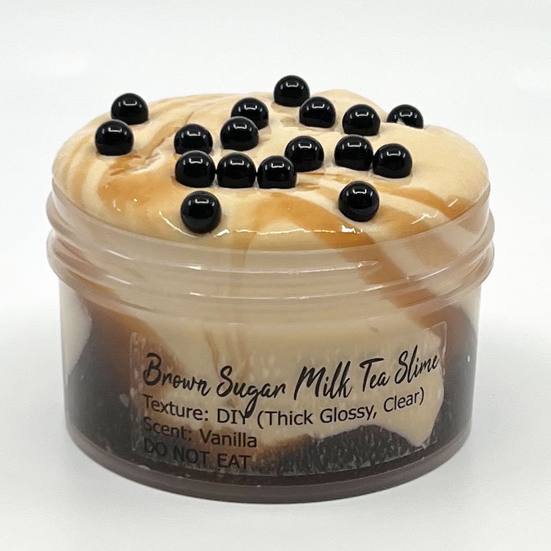 Puede incluir: Un tarro de slime de t&eacute; con leche y az&uacute;car moreno. El slime es una mezcla de colores marr&oacute;n y crema, cubierto con cuentas negras. El tarro tiene un recipiente de pl&aacute;stico transparente. El texto en el tarro dice "Brown Sugar Milk Tea Slime", "Texture: DIY".