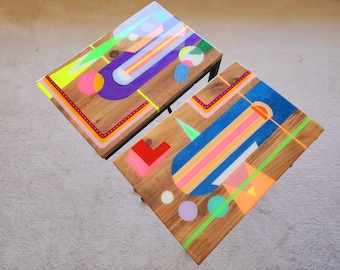 May include: Two wooden side tables with geometric designs painted in bright colors, including pink, blue, green, yellow, and purple. The tables have black metal legs.
