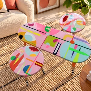 Hand painted colorful round and oval resin side tables with abstract geometric artwork and painted wooden legs in a modern living room.