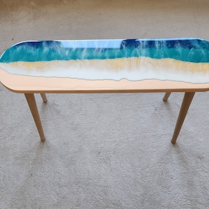 Pode incluir: Uma mesa longa e oval com uma base de madeira e um tampo de resina. O tampo de resina é azul, verde e branco, assemelhando-se a uma onda do oceano.