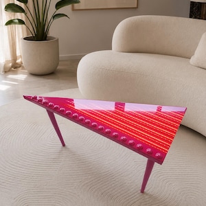 May include: A modern, triangular coffee table with a glossy, red and pink striped surface. The table has pink legs and is adorned with pink, rounded studs along the edges. The table is approximately 40 inches long.