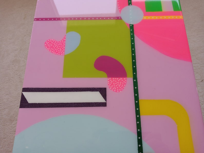 May include: Abstract geometric art print with pink, green, yellow, and blue shapes. The print features a white polka dot pattern on some of the shapes.