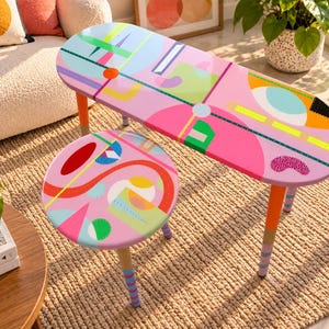 Hand painted colorful round and oval resin side tables with abstract geometric artwork and wooden legs in a modern living room.