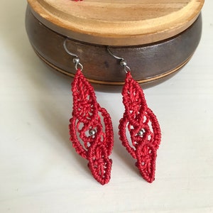 Puede incluir: Conjunto de joyas de macramé rojo con cuentas plateadas. El conjunto incluye una pulsera y un par de pendientes.