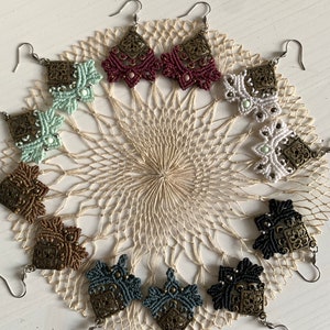 Peut inclure: Un ensemble de 10 paires de boucles d'oreilles en macramé faites à la main dans une variété de couleurs, notamment le vert, le blanc, le marron, le rouge et le bleu. Chaque boucle d'oreille est ornée d'un charme métallique décoratif.
