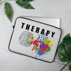 May include: A white laptop sleeve with the words "THERAPY ART" in black block letters. The design includes a brain illustration and colorful paint splatters. The sleeve is designed to fit a laptop.