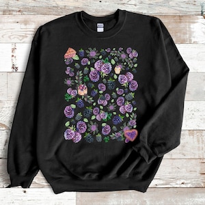 May include: Black sweatshirt with a watercolor design of purple blackberries, flowers, and leaves. The design includes a cupcake and a heart-shaped cookie. The sweatshirt is made of a soft material.