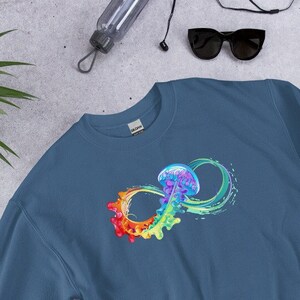 May include: A blue sweatshirt featuring a colorful infinity symbol with a jellyfish design. The jellyfish is depicted in shades of blue, purple, and green, while the infinity symbol transitions through a rainbow of colors. The sweatshirt is made of a soft material.