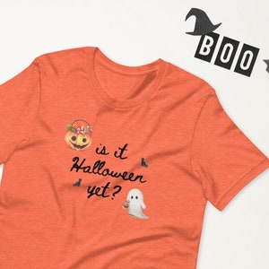 May include: Orange t-shirt with the phrase "is it Halloween yet?" and Halloween-themed graphics. The design includes a jack-o'-lantern, bats, and a ghost. The word "BOO" is spelled out with black letters. Pumpkins and bat cutouts are also visible.