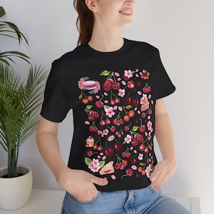 May include: A black t-shirt with a colorful print of cherries, flowers, and pastries. The print is a repeating pattern and covers the entire front of the shirt.