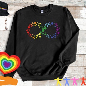 May include: Black sweatshirt featuring a colorful infinity symbol made of rainbow-colored dots. The design includes red, orange, yellow, green, blue, and purple hues. Additional rainbow-themed accessories are visible in the background.