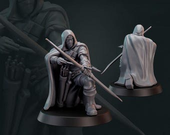 May include: A gray plastic miniature figurine of a hooded archer with a bow and arrow. The archer is kneeling and aiming the bow. The figurine is on a round base. The text "GALAAD" is visible in the background.