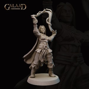 Puede incluir: Una figura miniatura de una mujer lanzando un hechizo. Lleva una túnica fluida y sostiene un bastón. La figura está hecha de plástico gris claro y mide unos 7,5 cm de alto.