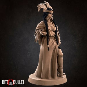 May include: A brown painted figurine of a woman wearing a long dress and a headdress with feathers. She is holding a small object in her hand.