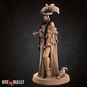 May include: A detailed figurine of a woman wearing a feathered headdress and a long flowing gown. She is holding a small object in her hand and a bird is at her feet.