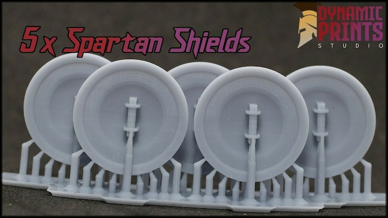 K&ouml;nnte beinhalten: F&uuml;nf graue, 3D-gedruckte Spartaner-Schilde mit einem erhabenen Design. Die Schilde sind an einer grauen Kunststoffbasis befestigt. Der Text "5 x Spartan Shields" ist oben im Bild sichtbar.