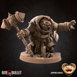 以下が含まれることがあります： 大きな頭と口の広い小さな人型生物のミニチュアフィギュアで、ローブを着てハンマーを持っています。フィギュアは茶色に塗られており、テクスチャのある表面のベースの上に立っています。画像の左下隅には「BITE THE BULLET」というテキストが表示されています。画像の右下隅には「(HAPPINESS NOISES)」というテキストが表示されています。