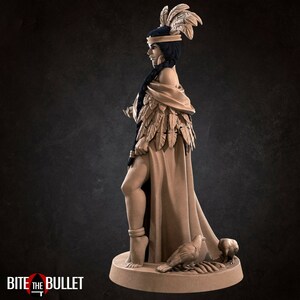 May include: A detailed figurine of a woman wearing a feathered headdress and a long robe. She is standing with her right leg slightly bent and her left leg straight. She is holding a small object in her right hand. Two birds are at her feet.
