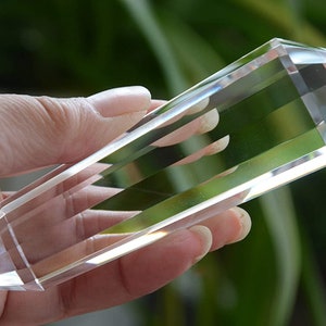 May include: A clear quartz crystal point, also known as a crystal wand, is held in a hand. The crystal is long and slender with a pointed tip. It is a popular tool for healing and meditation.