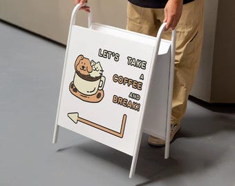 May include: A white A-frame sign with the text "LET'S TAKE A COFFEE AND BREAK!" and an illustration of a dog and cat in a coffee cup. The sign has a brown arrow pointing to the right and is being held by a person.