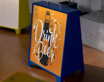 May include: A-frame sign with a blue frame and a handle. The sign features an orange background with a black beer bottle illustration and the words "Drink Beer" in white script. White paint splatters add a decorative touch.