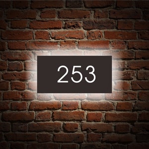 Puede incluir: Un letrero rectangular negro con texto blanco que dice "253" est&aacute; montado en una pared de ladrillo.