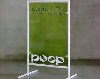 May include: A white metal sign with a green translucent panel. The sign reads "coffee?" with a coffee cup and hand symbol, and "open daily 7:30am-10pm." The word "peep" is displayed in large white letters at the bottom.