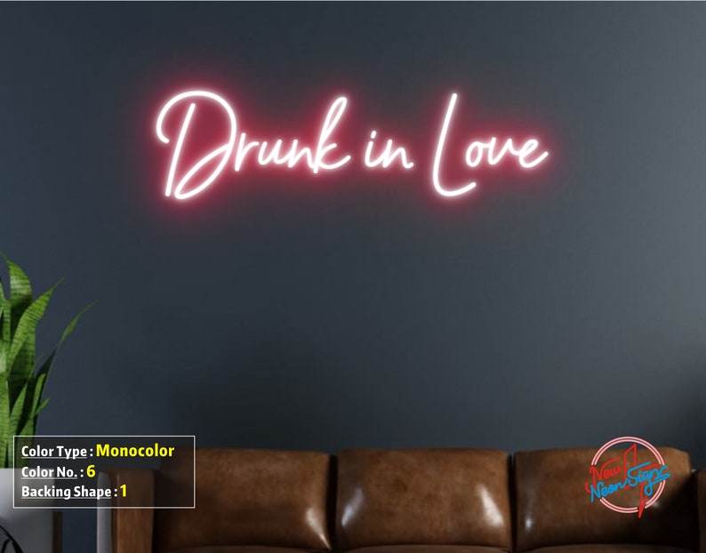 May include: Pink neon sign with the text "Drunk in Love" on a dark gray wall above a brown leather couch.