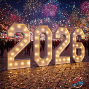 Może przedstawiać: Duże, podświetlane litery tworzące rok "2026", z żarówkami o ciepłym odcieniu, na tle fajerwerków i tłumu ludzi. Cyfry są białe. Scena rozgrywa się na brukowanym obszarze, z logo "New Neon Signs" w prawym dolnym rogu.