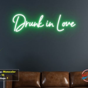 May include: Green neon sign with the text "Drunk in Love" on a dark gray wall. The sign is mounted above a brown leather couch.